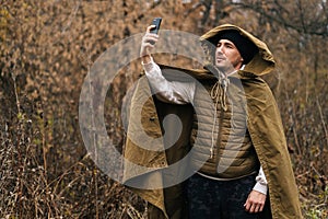 Portrait of survivalist male wearing tent raincoat searching for reception signal, making video call or recording video photo