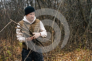 Portrait of survivalist male wearing warm clothes collecting dry deadwood for fire in forest on overcast cold day. photo