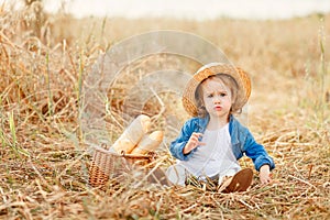 Portrait of a sweet beautiful little girl in straw hat sitting in a wheat field and makes a funny face. Happy childhood concept