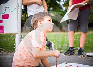 Portrait of sweet boy painting on white canvas into the park