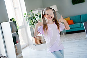 Portrait of sweet friendly girl toothy smile hands fingers demonstrate thumb up approval bright apartment indoors