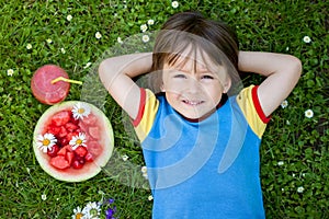 Portrait of sweet little boy, lying on the grass, fresh fruits a