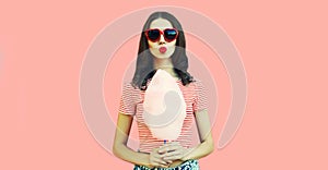 Portrait of sweet young woman blowing her lips sending air kiss with cotton candy wearing red heart shaped sunglasses on pink