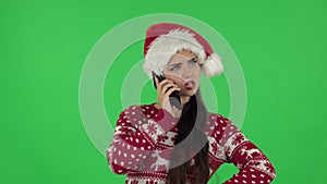 Portrait of sweety girl in Santa Claus hat is angrily talking for mobile phone. Green screen