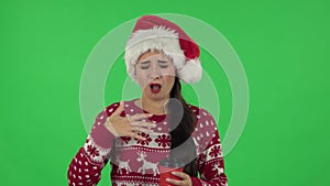 Portrait of sweety girl in Santa Claus hat is drinking unpalatable coffee. Green screen