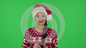 Portrait sweety girl in Santa Claus hat seductively smiling and gesture threatens by shaking index finger. Greenscreen