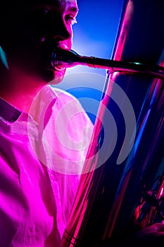 Portrait of talented musician seated, playing trumpet with soft blue-pink stage lights. Classical symphony.