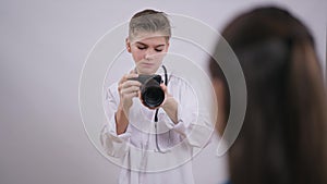 Portrait of talented teenage boy taking photo with camera thinking standing at white background. Unrecognizable girl