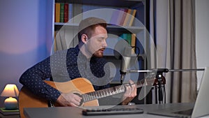 Portrait of talented young guitarist singer man playing guitar and singing into microphone while recording song in home