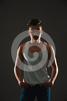 Portrait of a tanned cheeky guy with a fashionable hairstyle on a gray background. A man in a T-shirt and jeans.