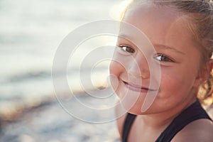 Portrait of a tanned little girl in the rays of the sun against the background of the sea