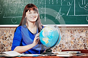 Portrait of teacher.beautiful young woman in a blue dress sits at a desk with a globe on the background of a board