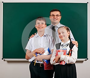 Portrait of a teacher, schoolboy and schoolgirl posing with exercise books, pens, pencils and other school supplies on blackboard