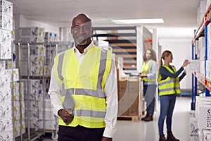 Portrait Of Team Leader With Digital Tablet In Warehouse With Staff Picking Items From Shelves 