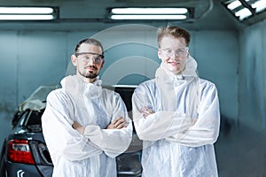 Portrait of a team of two young men of professional car painter with protective clothing standing next to a car in front of a car
