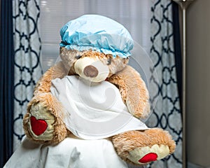 A portrait of a teddy bear dressed in a towel and wearing a shower cap. Wide angle view