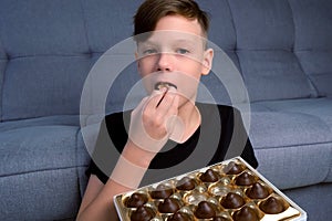 Portrait of teen boy is eating chocolate candies from gift box and enjoying it.