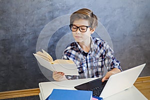 Teen boy reading book and use laptop at home