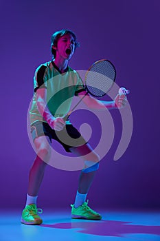 Portrait of teen boy in uniform, badminton player after successful game over blue purple background in neon ligth