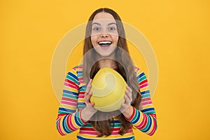 Portrait of teen child girl hold citrus fruit pummelo or pomelo, big grapefruit isolated on yellow background. Excited