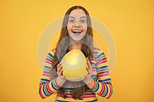 Portrait of teen child girl hold citrus fruit pummelo or pomelo, big grapefruit  on yellow background. Excited