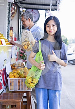 teen girl carry net tole bag with fruits doing thumb up at community fruits store for using environmentally friendly bags photo