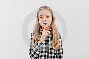 Portrait of teen girl shushing, showing shhh, taboo sign, press finger to lips with concerned face, keep quiet, stands over white