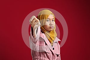 Portrait of teenage asian muslim girl looked disappointed while showing thumbs down gesture