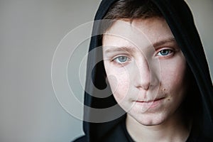 Portrait of a teenage boy with blue eyes and pursed lips. The boy in the black hood