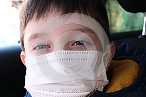 A portrait of teenage boy in a car wearing white surgical medical face mask as a protection against virus disease, coronavirus