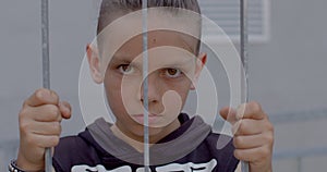 Portrait teenage boy hands holding on bars. He carefully looks in camera.