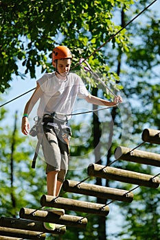 Portrait of teenage boy having fun at outdoor extreme adventure rope park. Active childhood, playing outdoors.