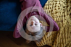 Portrait teenage boy lying on sofa upside down with hands behind head and looking camera