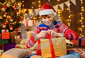 Portrait of teenage boy in new year decoration. He has a gift box, has fun and a great mood. Holiday lights, gifts and christmas