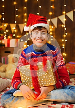 Portrait of teenage boy in new year decoration. He has a gift box, has fun and a great mood. Holiday lights, gifts and christmas