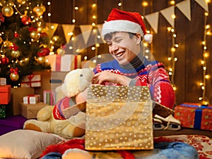 Portrait of teenage boy in new year decoration. He opening a gift box, has fun and a great mood. Holiday lights, gifts and