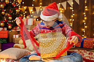 Portrait of teenage boy in new year decoration. He opening a gift box, has fun and a great mood. Holiday lights, gifts and