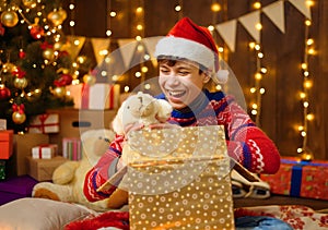 Portrait of teenage boy in new year decoration. He opening a gift box, has fun and a great mood. Holiday lights, gifts and