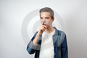 Portrait of teenage boy picking nose, standing over white background