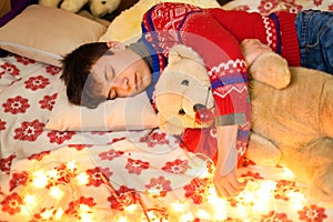 Portrait of teenage boy sleeping in new year or christmas decoration. Holiday lights, gifts and christmas tree decorated with toys