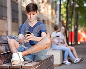 Portrait of teenage boy using smartphone on the bench at day outdoor