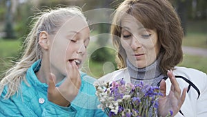 Portrait of teenage caucasian blond girl talking to the older woman with a bouquet of wildflowers. Cheerful women