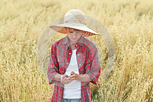 Portrait of teenage farmer boy is checking oat seeds in cupped palms at ripe field