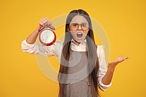 Portrait of teenage girl with clock alrm, time and deadline. Studio shot isolated on yellow background. Angry face