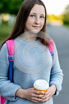 Portrait of a teenage girl close-up. Summer in nature. In the hands of a hot cup of coffee or tea. Behind the backpack