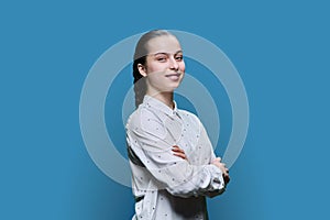 Portrait of teenage girl with crossed arms on blue background