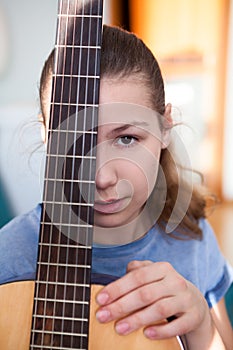 Portrait of teenage girl guitarist with fretboard of guitar, looking at camera