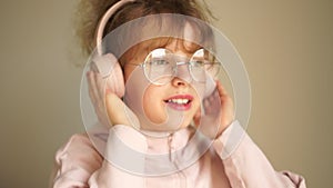 Portrait of a teenage girl with headphones on her head, wearing glasses. Girl listens to music on headphones and dances