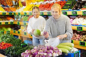 Portrait of teenage girl and her mother who buying fresh vegetables and fruits at shop
