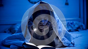 Portrait of teenage girl lying under blanket and reading book